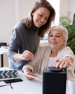Persona gran acompanyada d'una noia que li ensenya l'ajuda tecnològica de casa