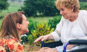 Hija sonriendo a madre mayor en silla de ruedas